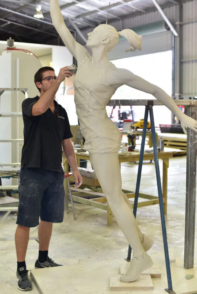 Artist creating a large bronze sculpture of a female athlete in dynamic jumping pose inside an industrial workshop. Bronze sculptures in progress.
