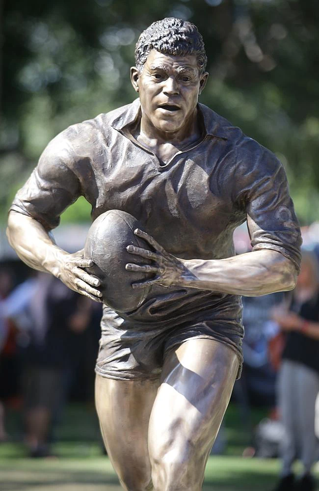 Bespoke Bronze Memorial: Bronze statue of a rugby player in action, holding a ball, outdoors with blurred trees and people in the background.